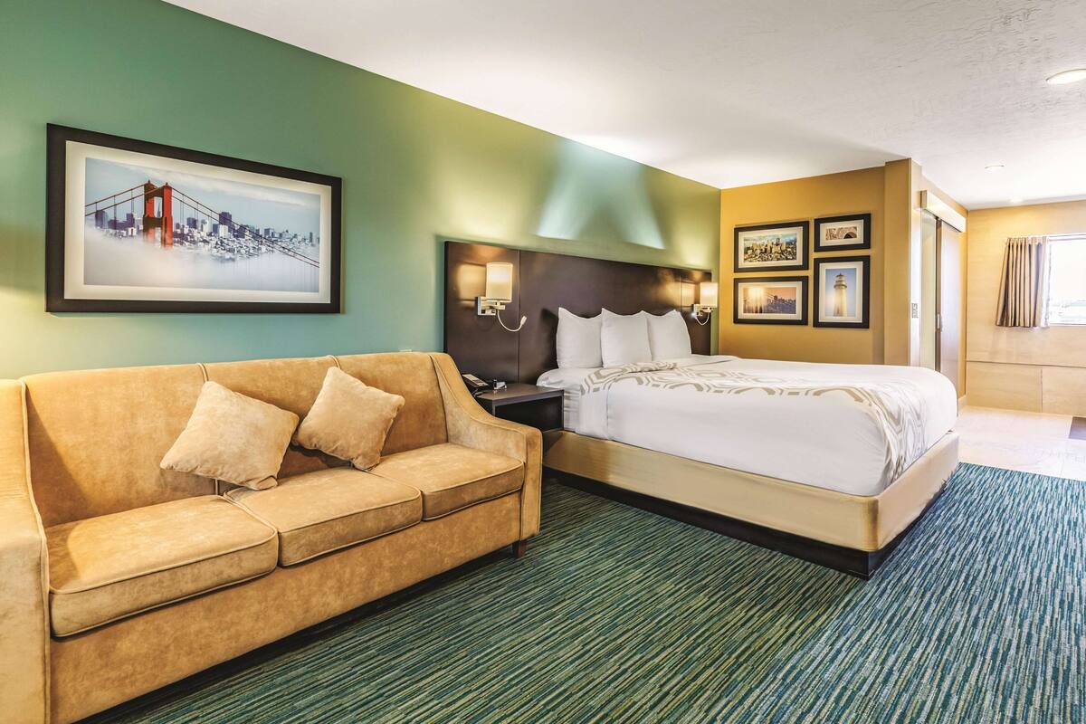 Una habitación de hotel con cama, sofá, mesita de noche y una pared decorada con cuadros.