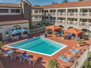 A hotel with a swimming pool, outdoor seating, and a covered area with umbrellas.