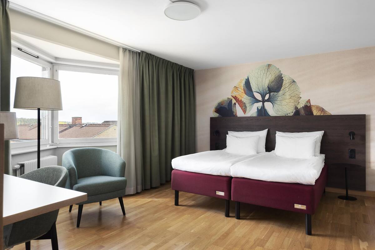 A hotel room with a bed, a chair, a table, a lamp, and a window with curtains.