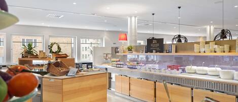 Zona buffet moderna con frutas y verduras variadas, mostradores de madera y un interior luminoso.