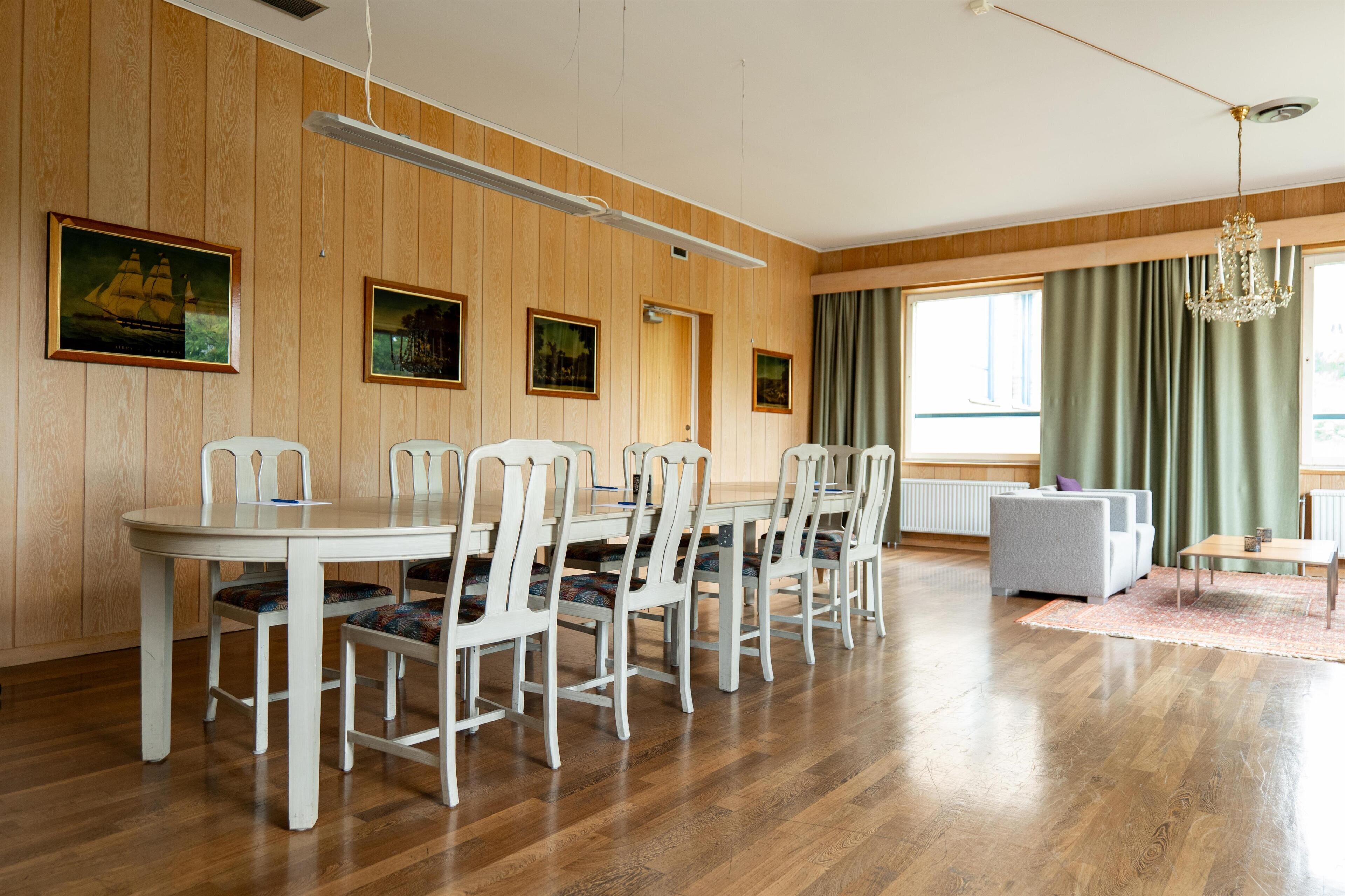Un comedor con pared revestida de madera, una mesa de comedor blanca con sillas y un sofá gris.