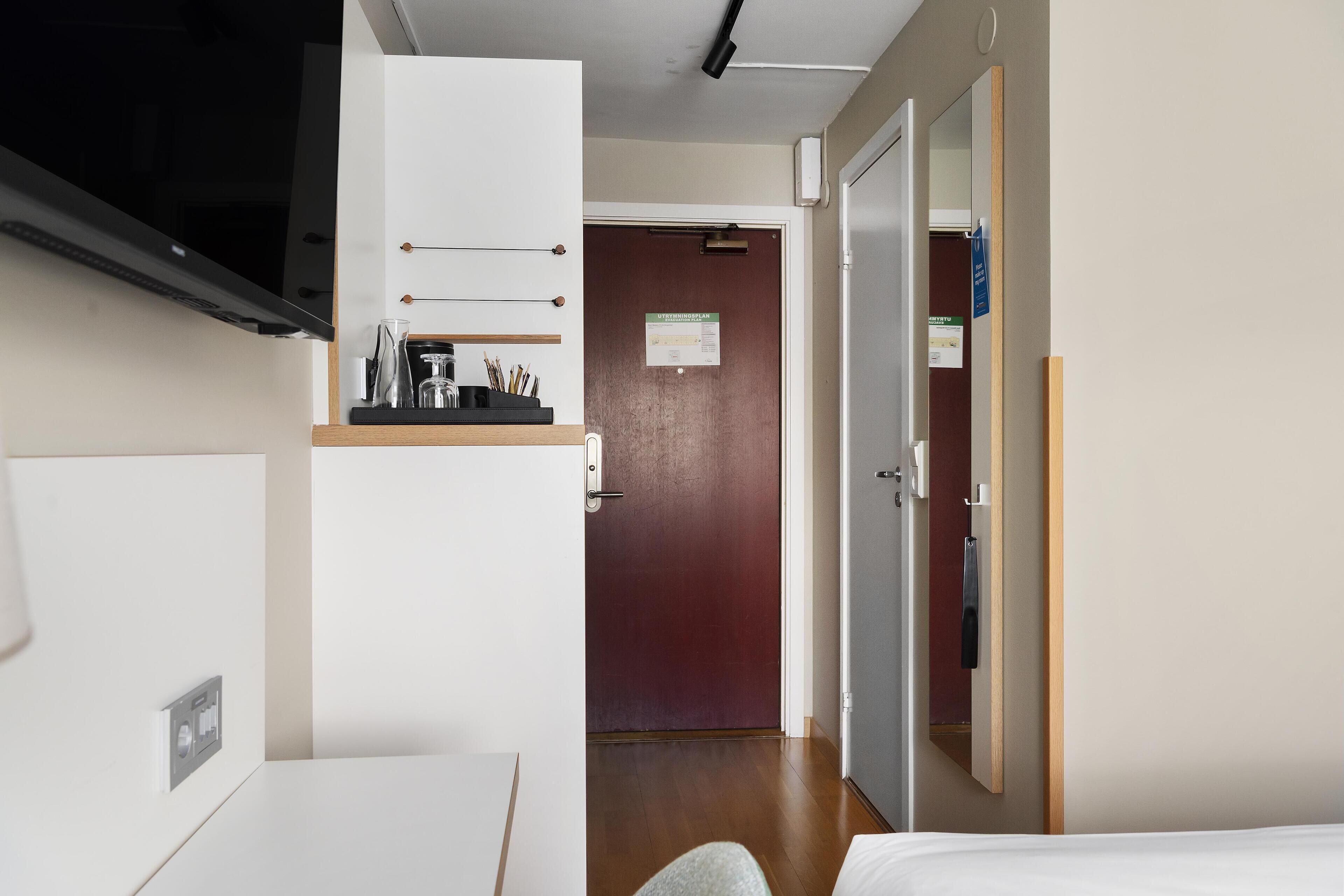 A hotel room with a bed, a desk, a TV, a wardrobe, and a door leading to another room.