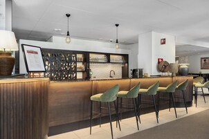 A bar area with wooden counter, green bar stools, hanging pendant lights, and a menu board.