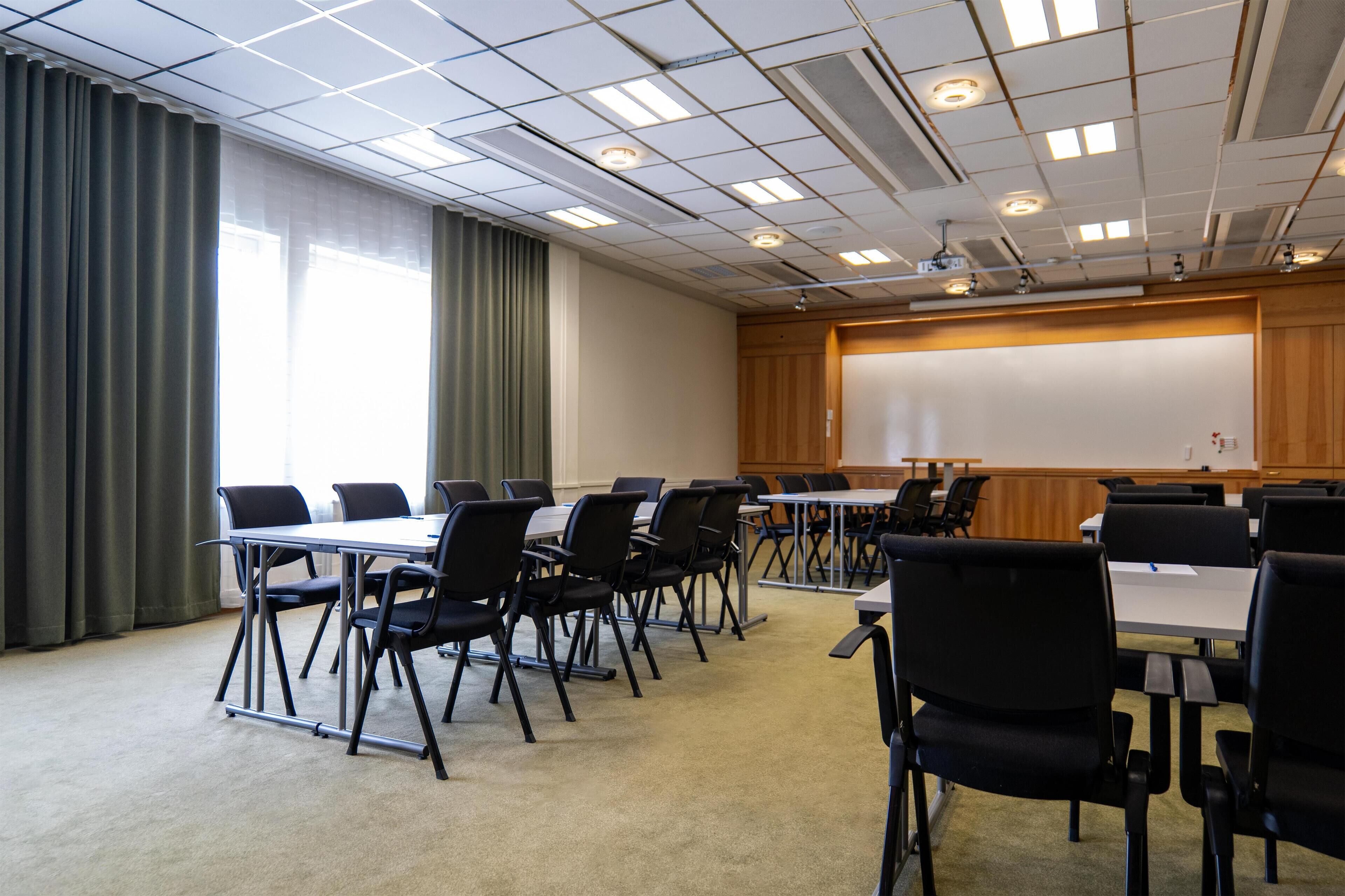 Un salón de conferencias con una pizarra grande, varias mesas y sillas negras.