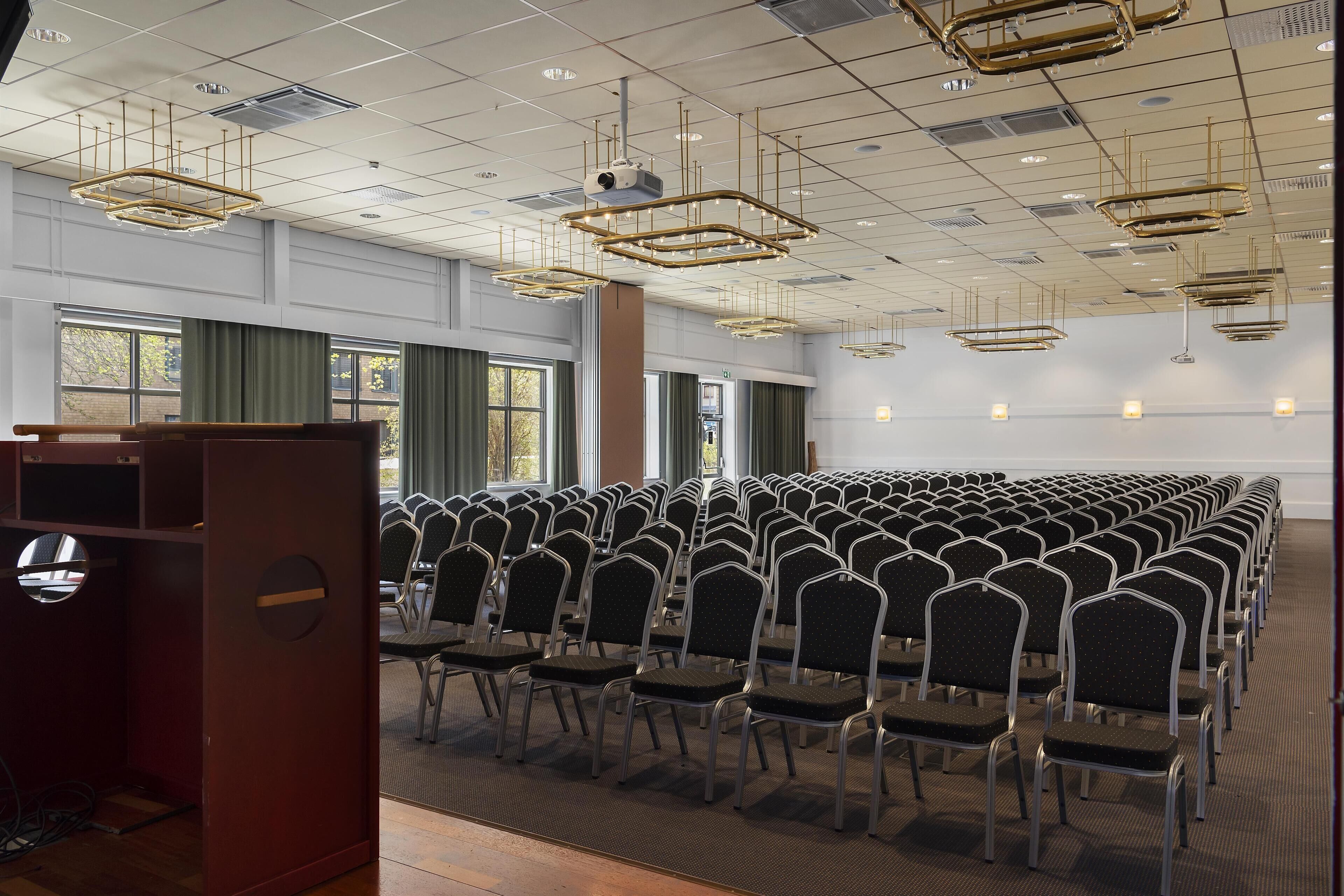 A conference room with rows of chairs, a podium, and modern chandeliers.