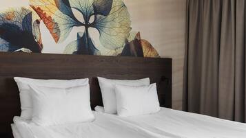 A neatly made bed with white linens, a wooden headboard, and a large abstract wall art piece.
