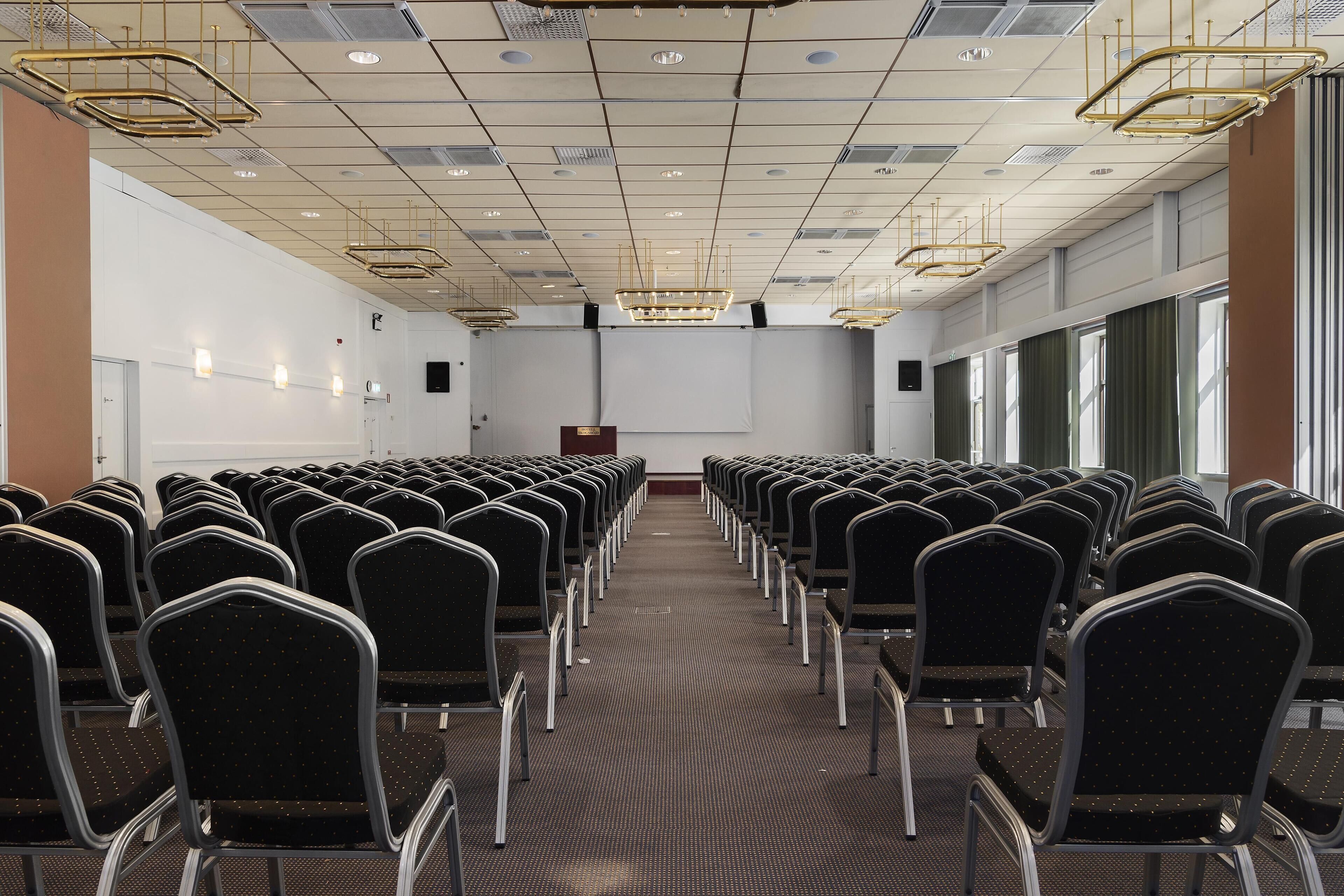 A conference room with rows of chairs, a projector screen, and a podium.