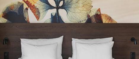 A bed with white bedding, a wooden headboard, and a wall-mounted light fixture.