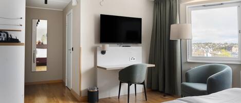 A hotel room with a bed, a desk with a TV, two chairs, a window with a view, and a door leading to another room.