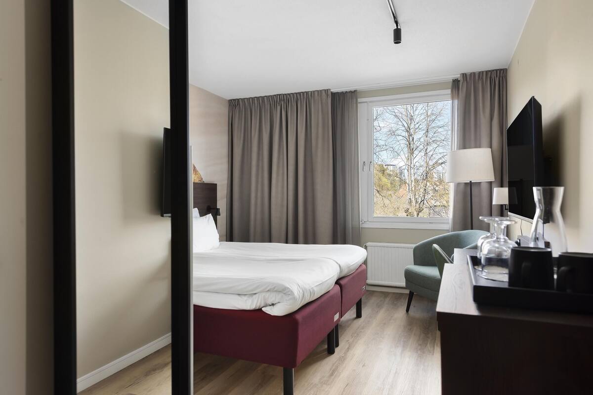 A hotel room with a bed, a desk, a chair, a TV, and a window with curtains.