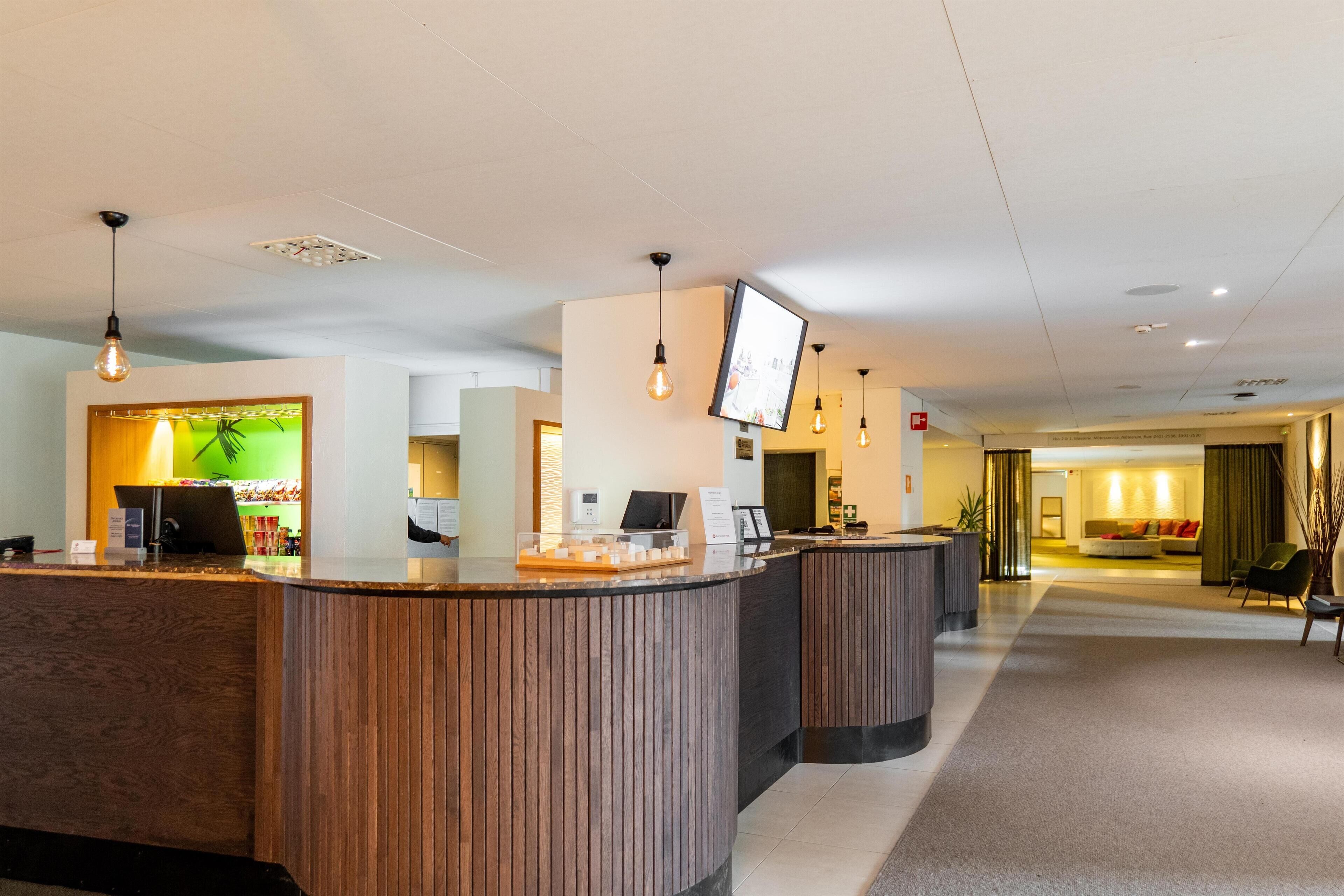 Un área de recepción con mostradores de madera, una pared verde con planta y un televisor de pantalla plana montado.
