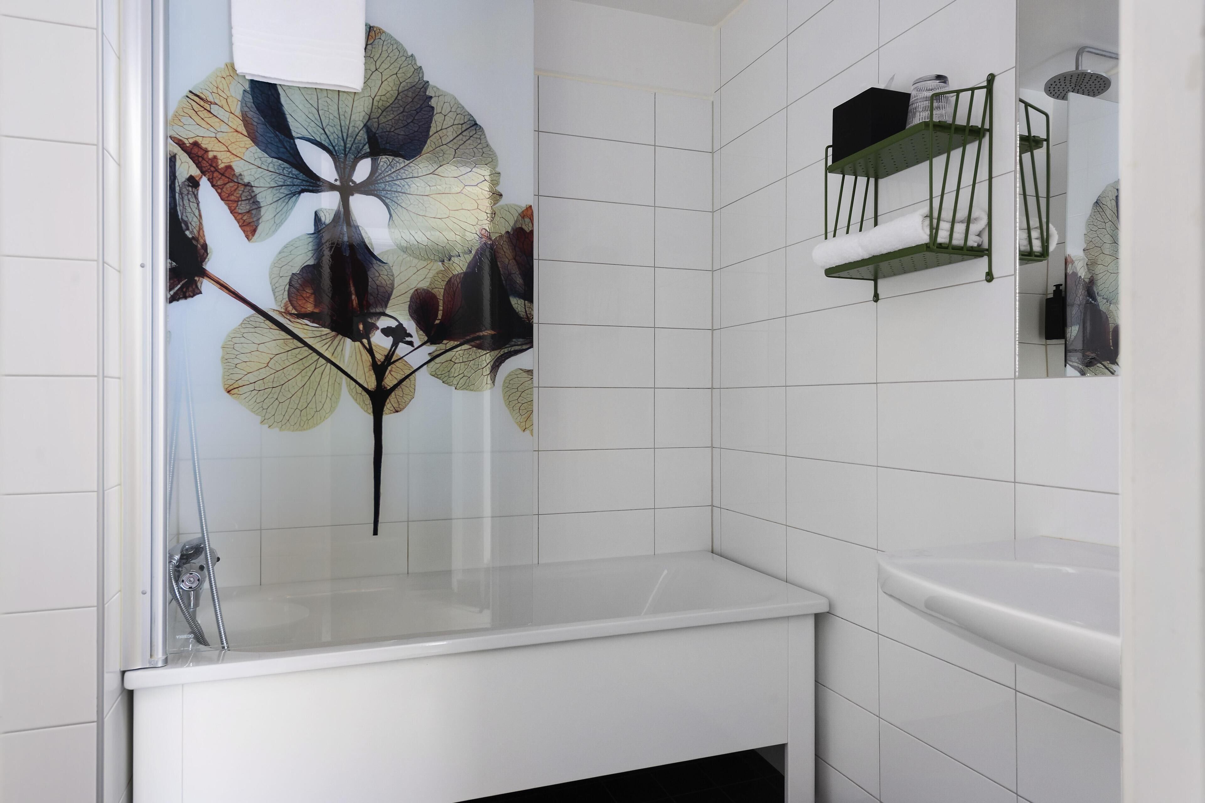 Een badkamer met witte tegels, een glazen douchecabine, een witte wastafel en een handdoekrek.