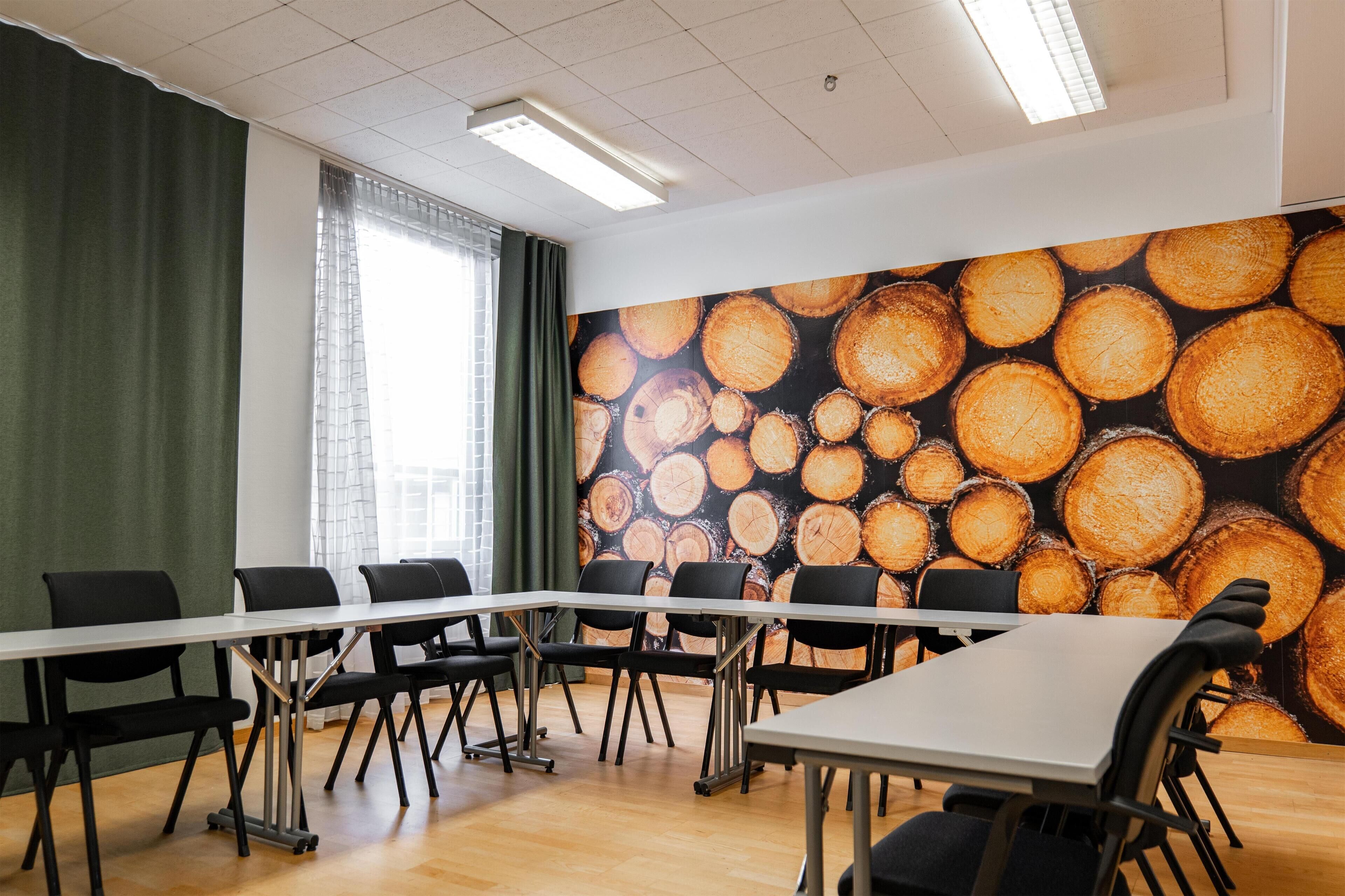 Un salón de conferencias con una larga mesa y sillas, un ventanal con cortinas y una pared con textura de madera.
