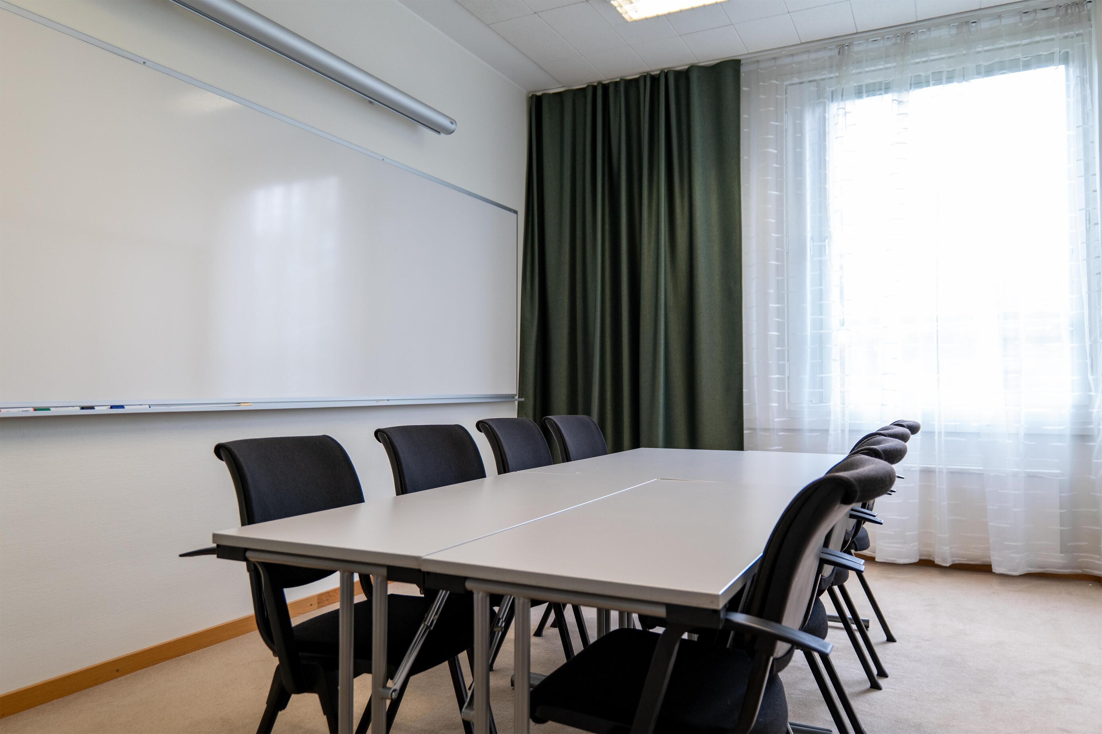 A conference room with a whiteboard, a long table, and black chairs.