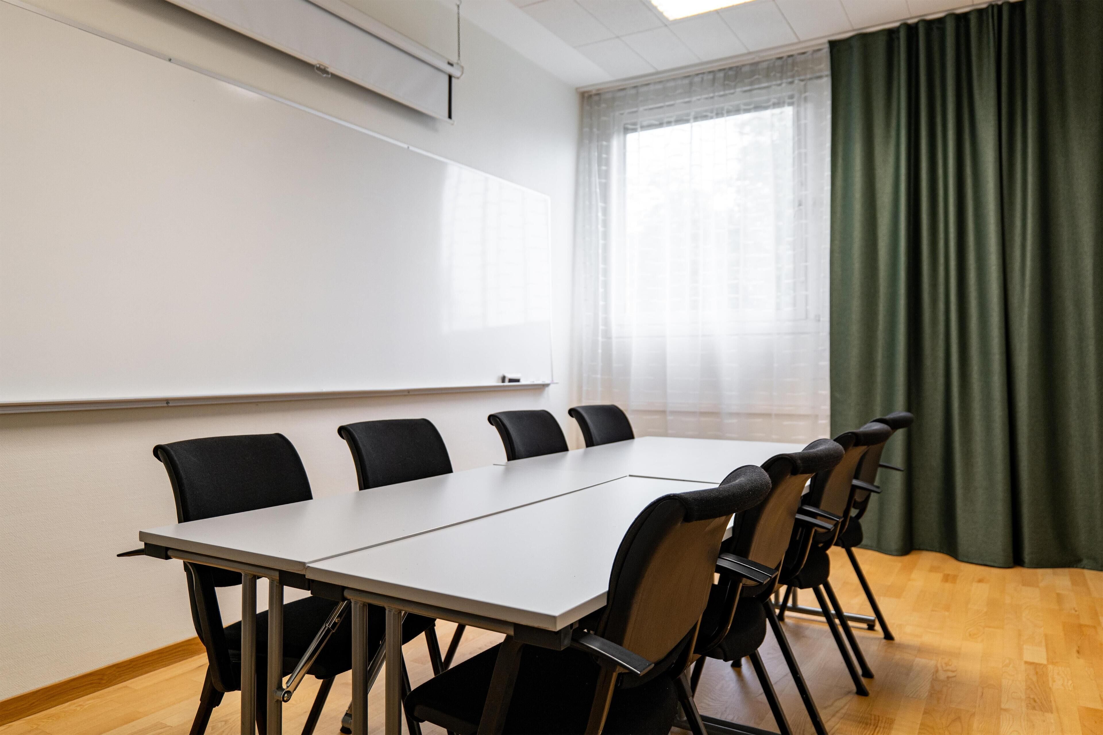Un salón de conferencias con una pizarra, una mesa larga y seis sillas.