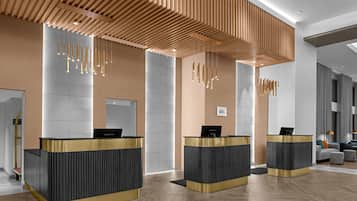 A modern reception area with three reception desks, wooden slatted ceiling, and a seating area with a sofa and ottoman.