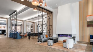 A modern lounge area with a sofa, ottoman, and chairs, a fireplace, and a dining area with tables and chairs. -  Delta Hotels by Marriott Santa Clara (Santa Clara)