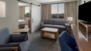 Ein Hotelzimmer mit Bett, einer Couch, einem Fernseher, einem Schreibtisch und Blick auf die Stadt.