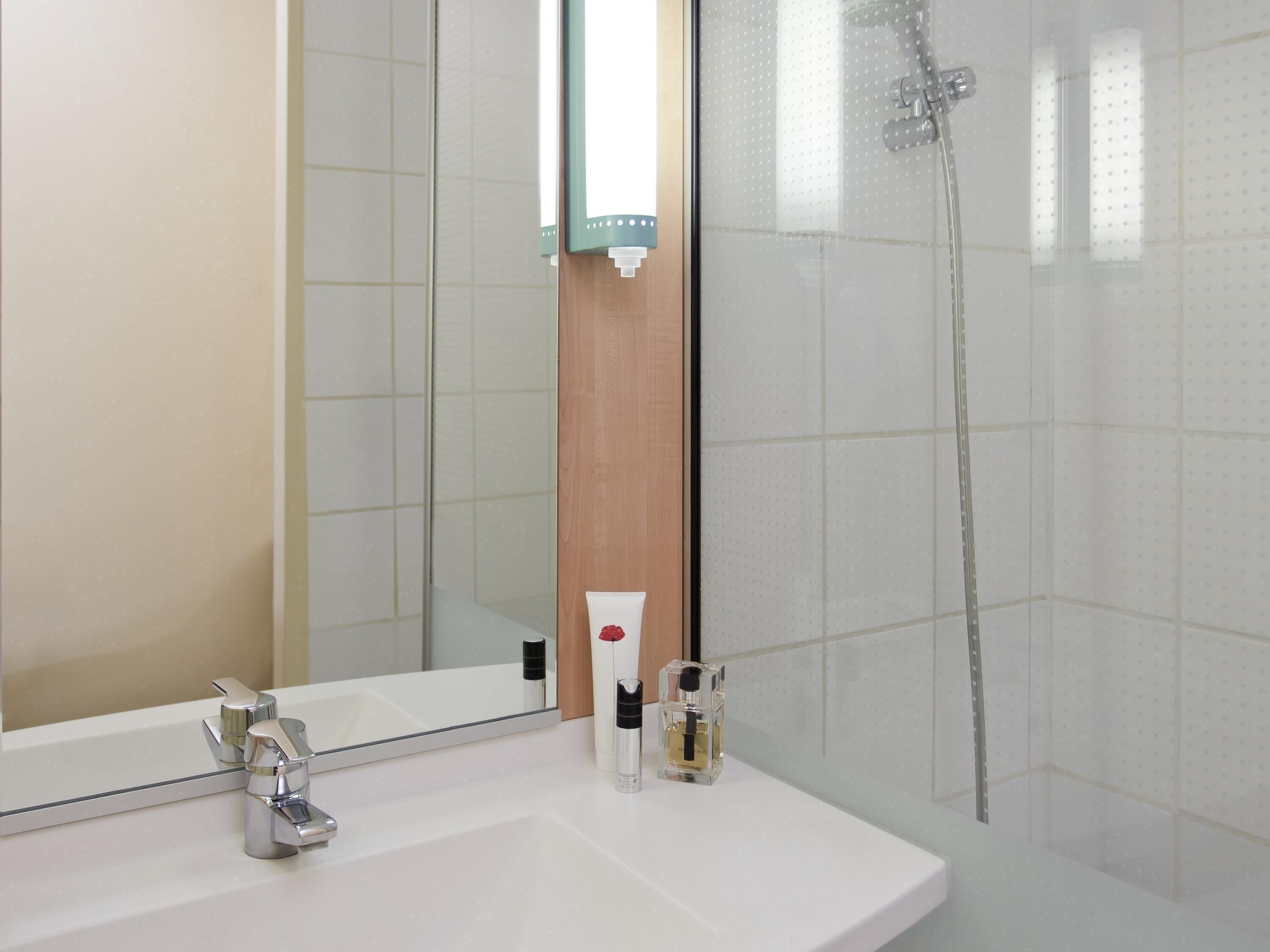 A modern bathroom with a large mirror, a white sink, a shower, and a wooden panel.