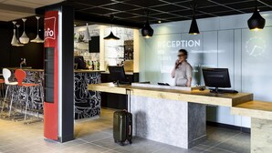 A reception desk with a modern design, a bar area with stools, and a clock on the wall. - ibis Roanne (Le Coteau)