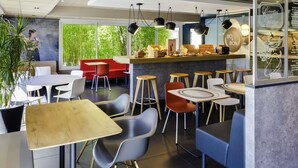A modern cafe interior with tables, chairs, and a counter. - ibis Roanne (Le Coteau)