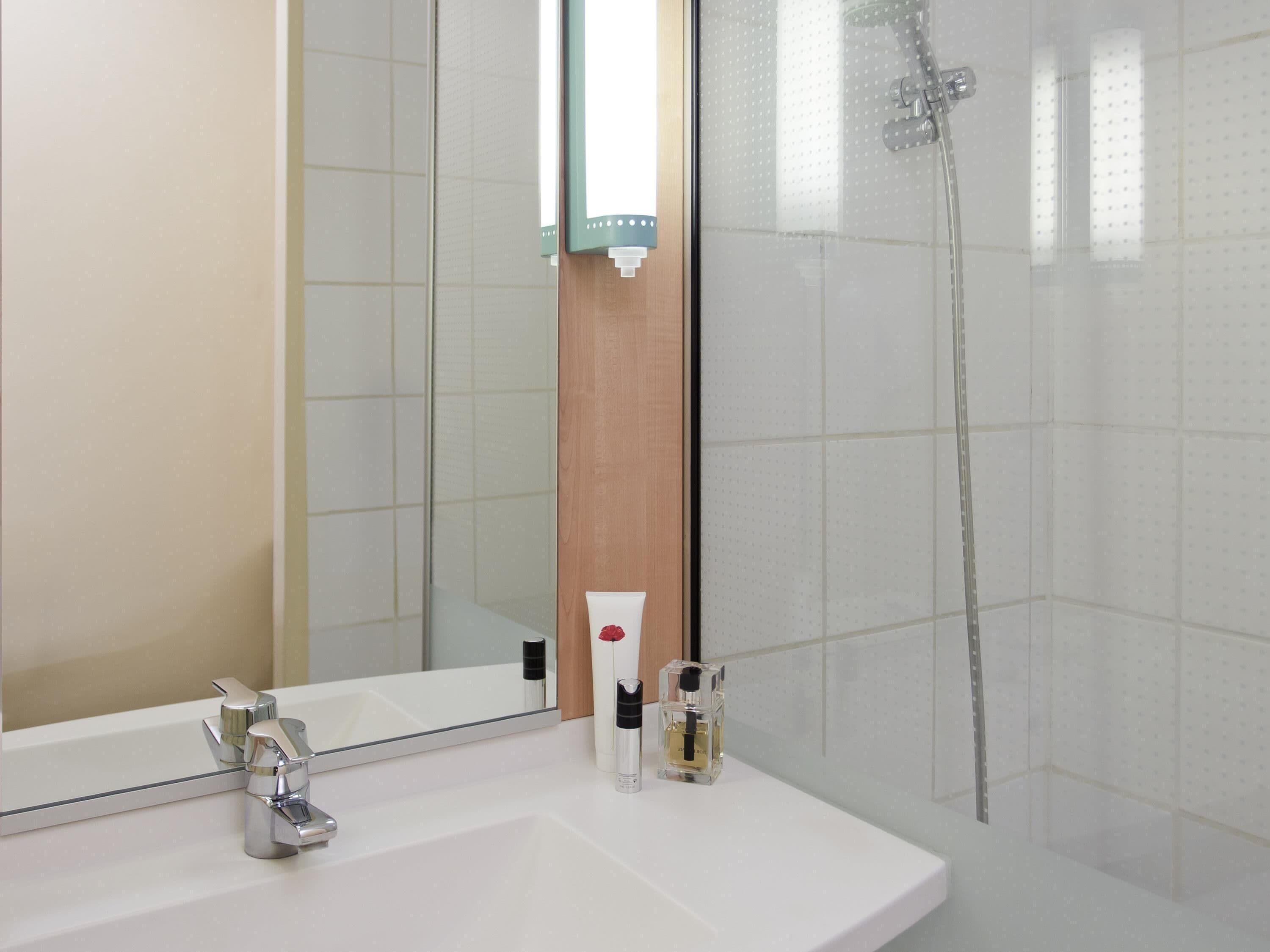 Un baño moderno con un espejo grande, un lavamanos blanco, una ducha y un panel de madera.