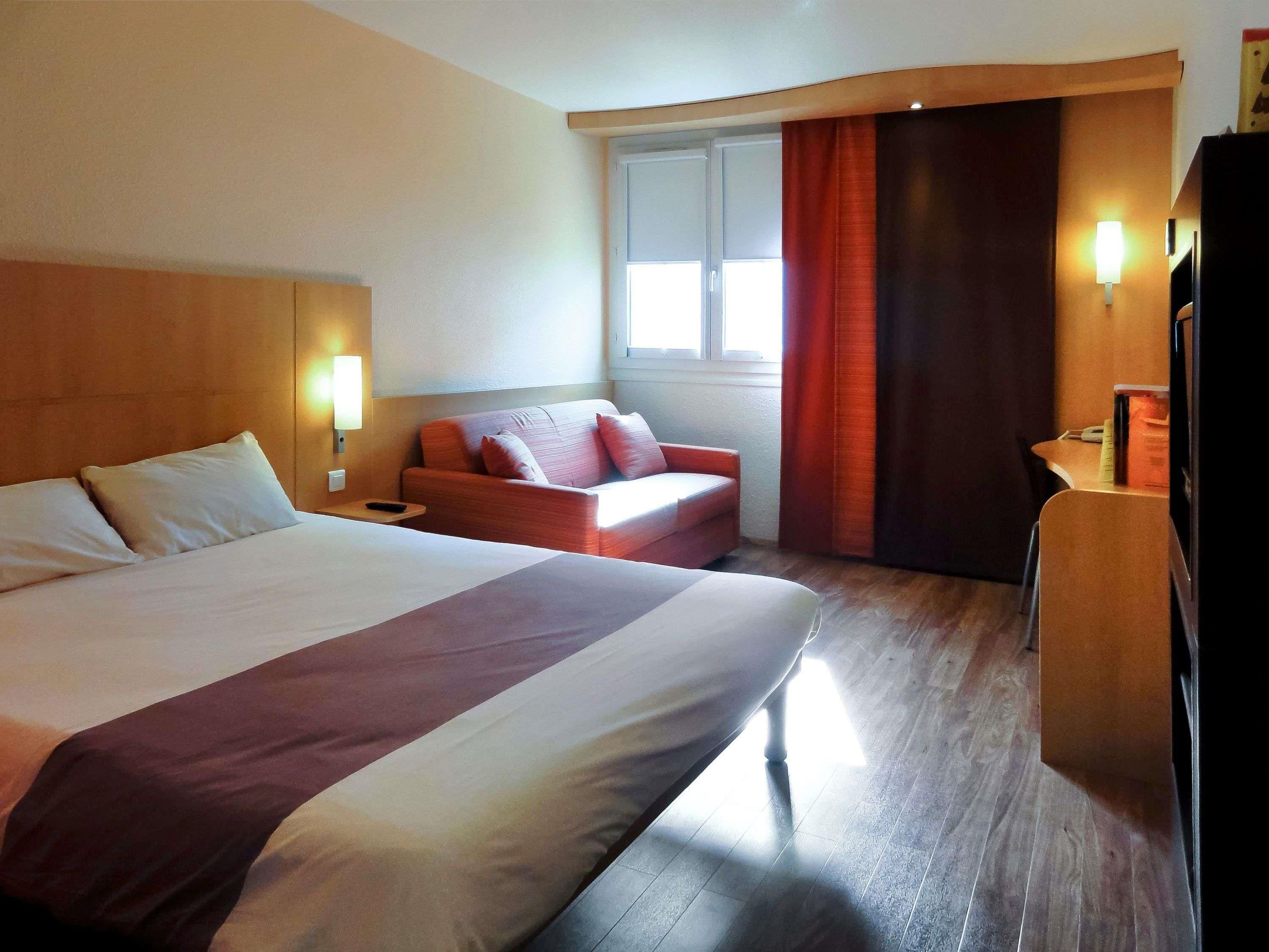 A hotel room with a large bed, a sofa, a desk, and a window with curtains.
