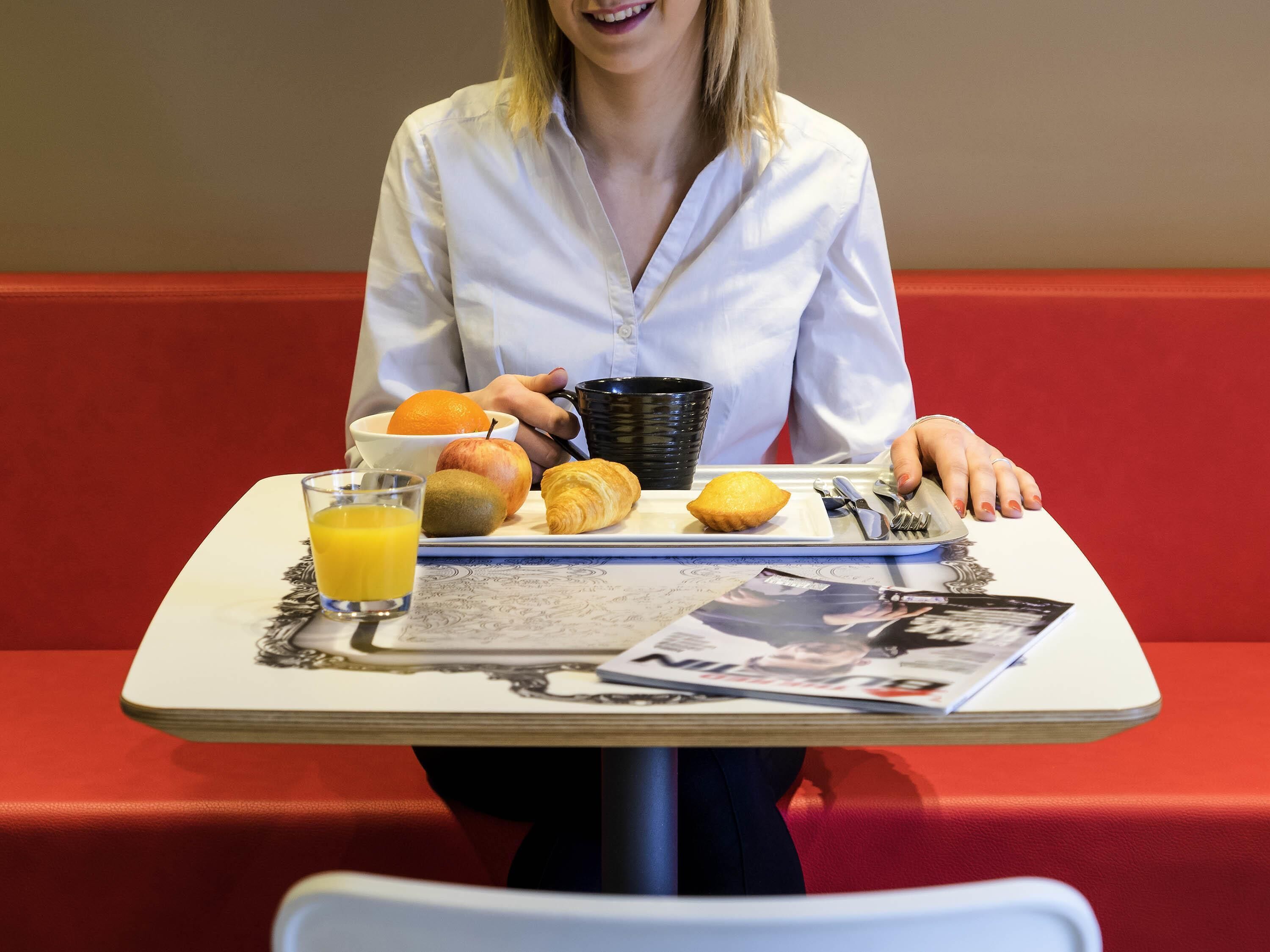 A person seated at a table with a meal consisting of fruit, a croissant, and a muffin, along with a glass of orange juice.