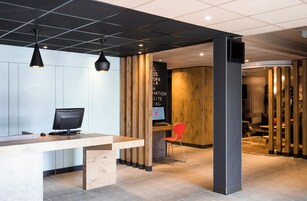 Uma área de recepção moderna com um balcão de madeira, um computador e uma cadeira vermelha.