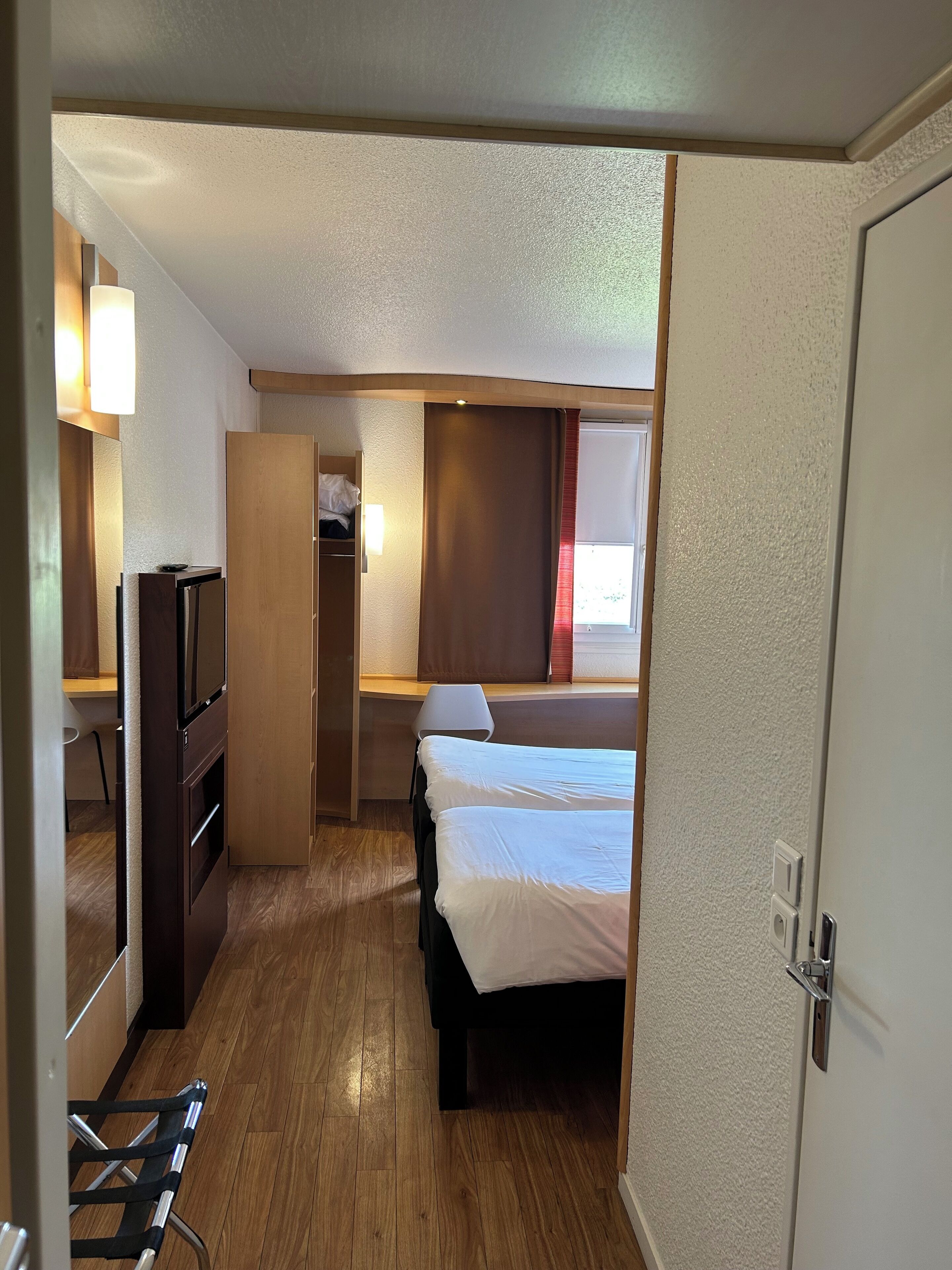 Una habitación de hotel con cama, escritorio, armario y televisor.