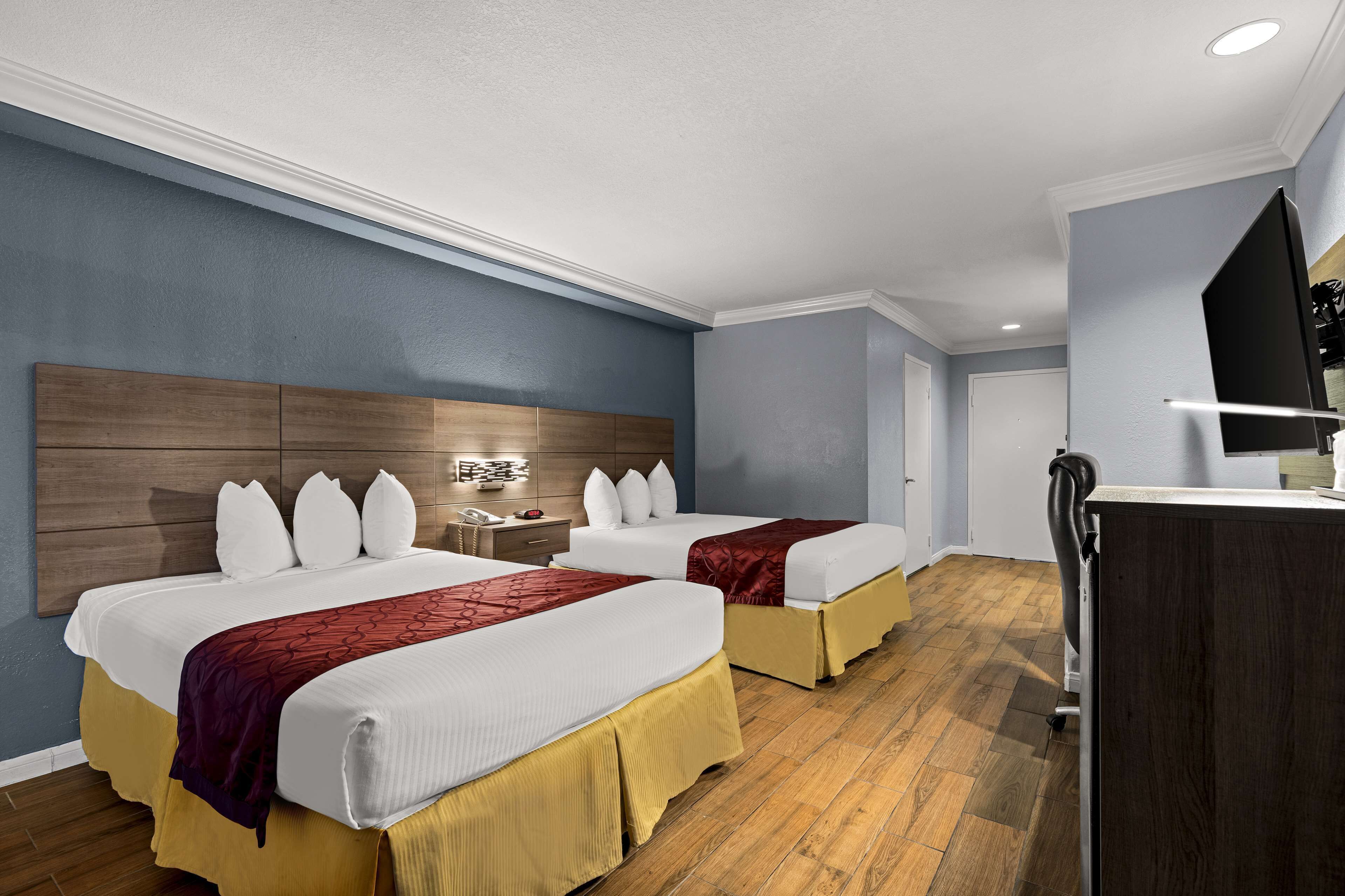 Habitació d'hotel amb dos llits, una taula de treball, televisió i un panell de capçalera de fusta.