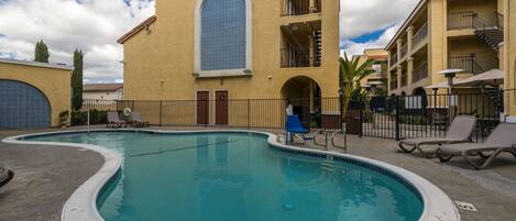 Una piscina con sillas de descanso y un edificio con un gran ventanal arqueado y balcones.