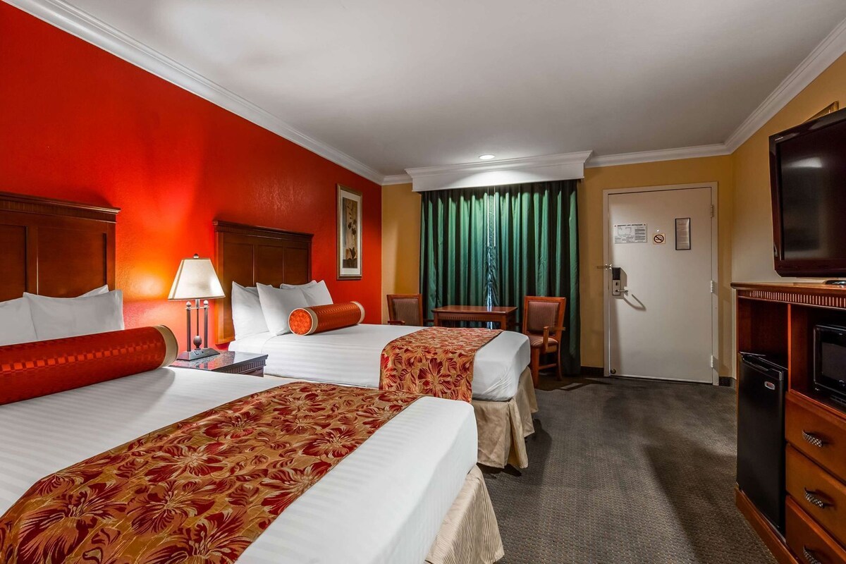 A hotel room with two beds, a desk, a chair, a television, and a door with a sign.