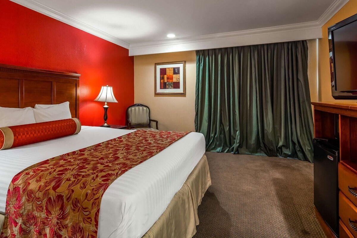 A hotel room with a large bed, a wooden headboard, a desk with a television, and a green curtain.