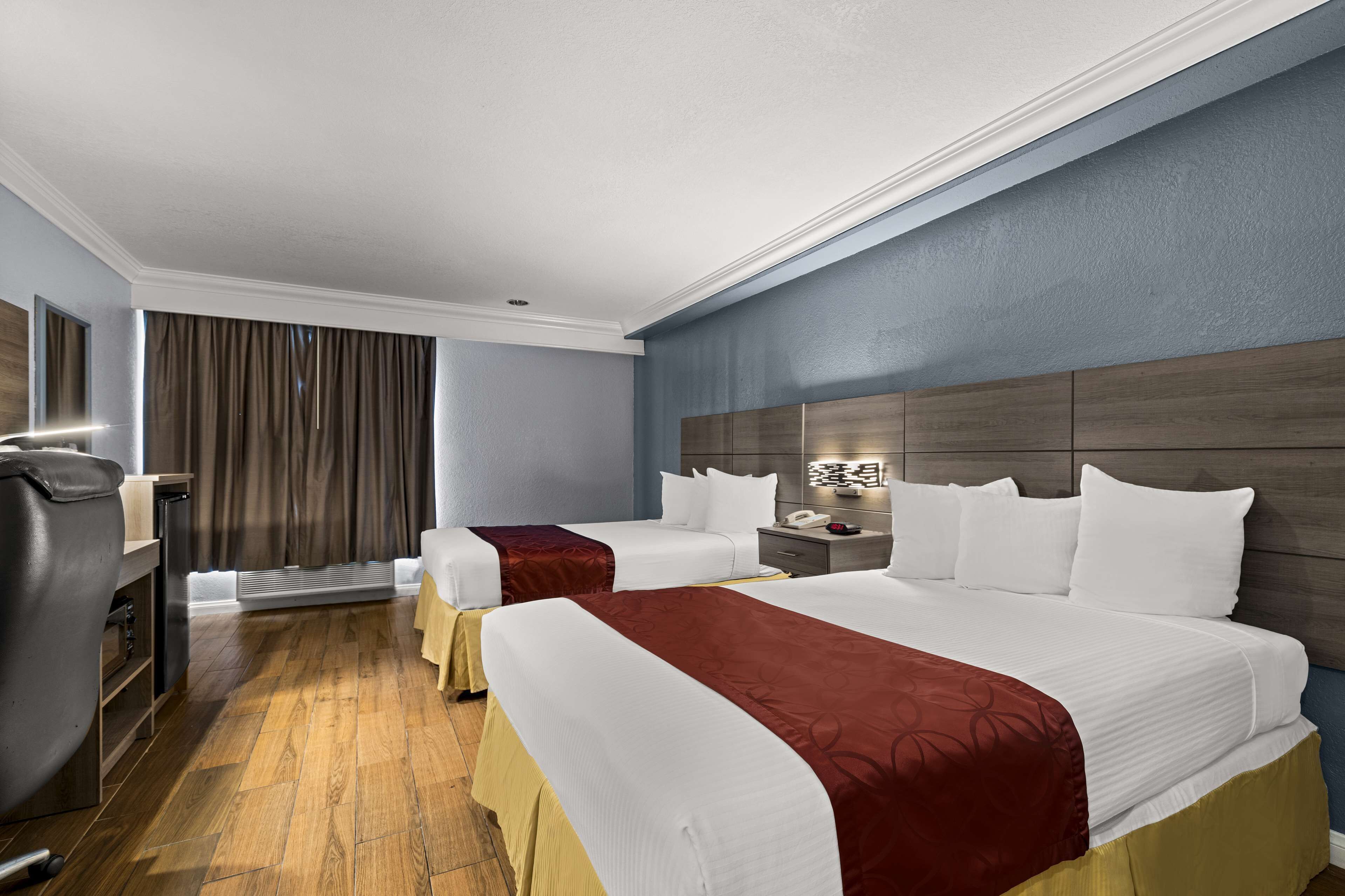 Habitación de hotel con dos camas, un escritorio, una silla y un ventanal con cortinas.