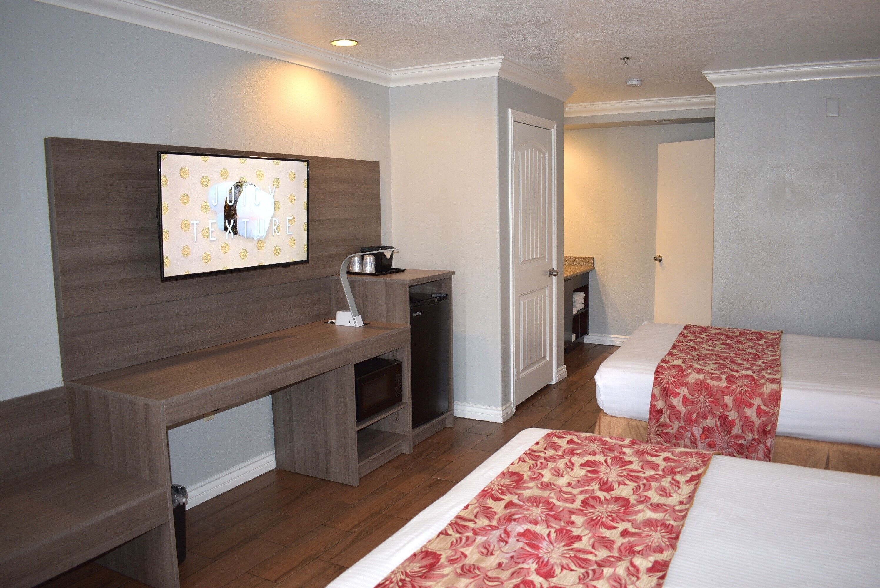 Una habitación de hotel con dos camas, un escritorio de madera, un televisor de pantalla plana y una pequeña cocina americana.