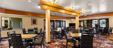 A spacious dining area with multiple tables and chairs, a patterned carpet, and large windows allowing natural light.