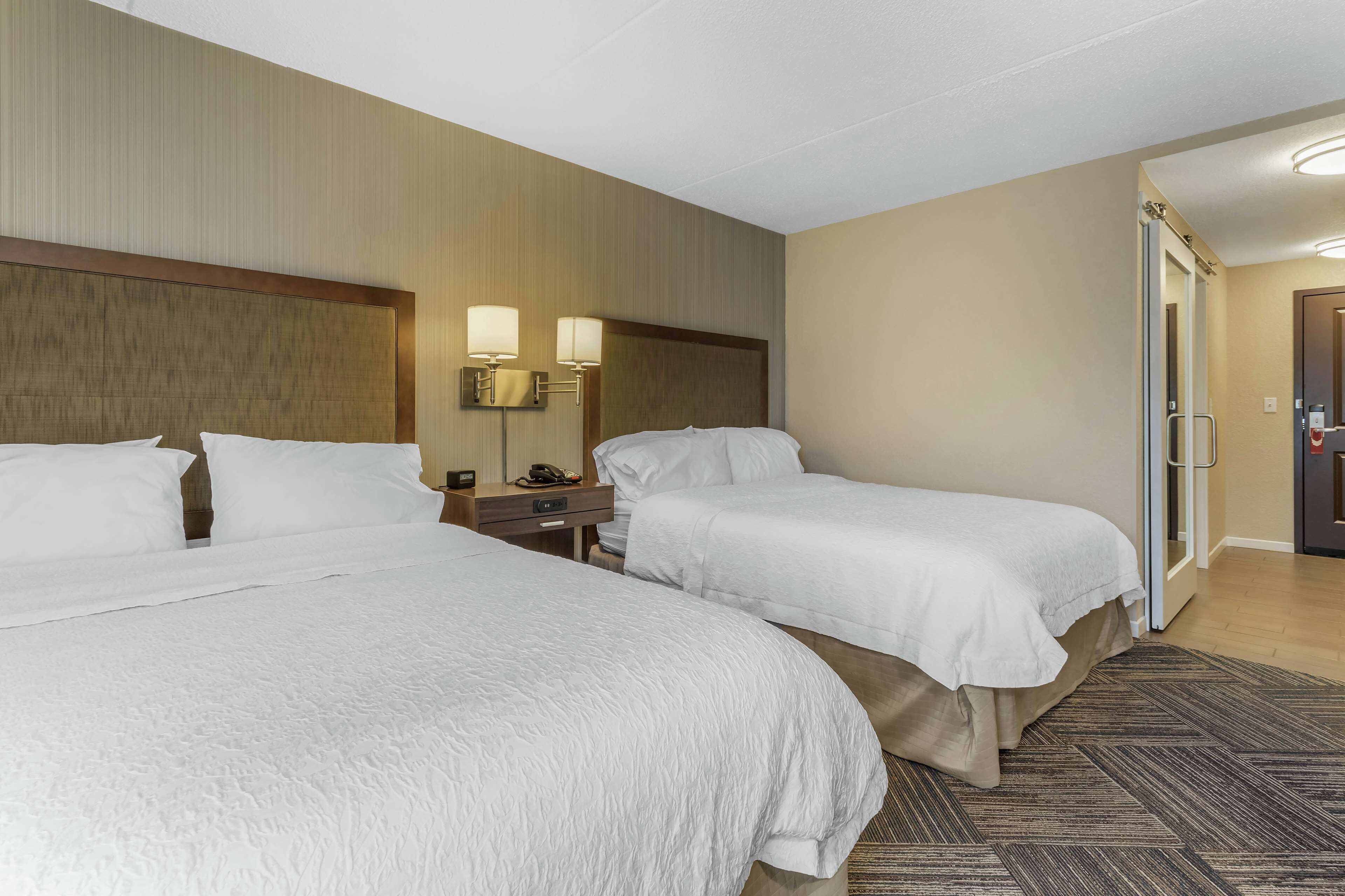 Habitación de hotel con dos camas, una mesita de noche y una lámpara.