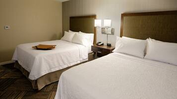 A hotel room with two beds, a bedside table with a lamp, a phone, and a brown folder on the left bed.