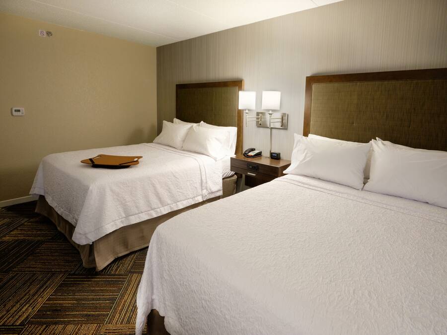 A hotel room with two beds, a bedside table with a lamp, a phone, and a brown folder on the left bed.