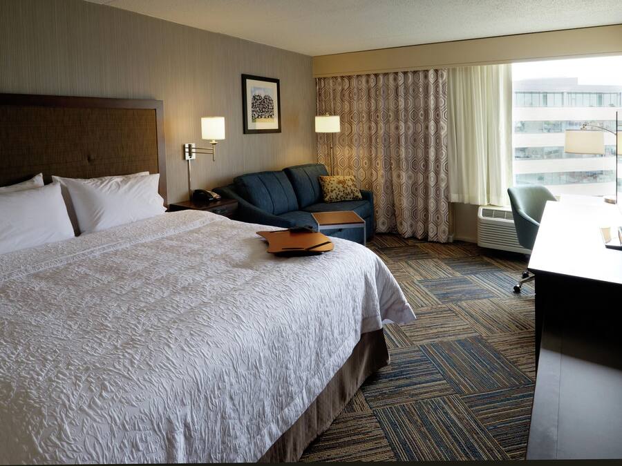 A hotel room with a large bed, a sofa, a desk, and a view of the city.