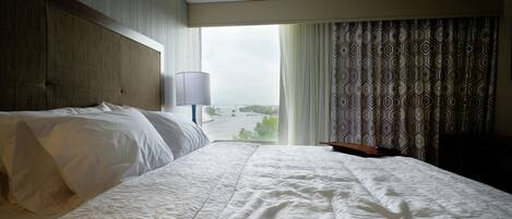 Habitación de hotel con una cama grande, cabecera, ventana con cortinas y vistas al exterior.