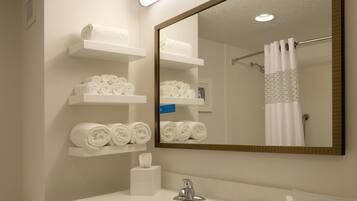 Une salle de bain avec un lavabo blanc, un miroir et des étagères où sont soigneusement pliées des serviettes.