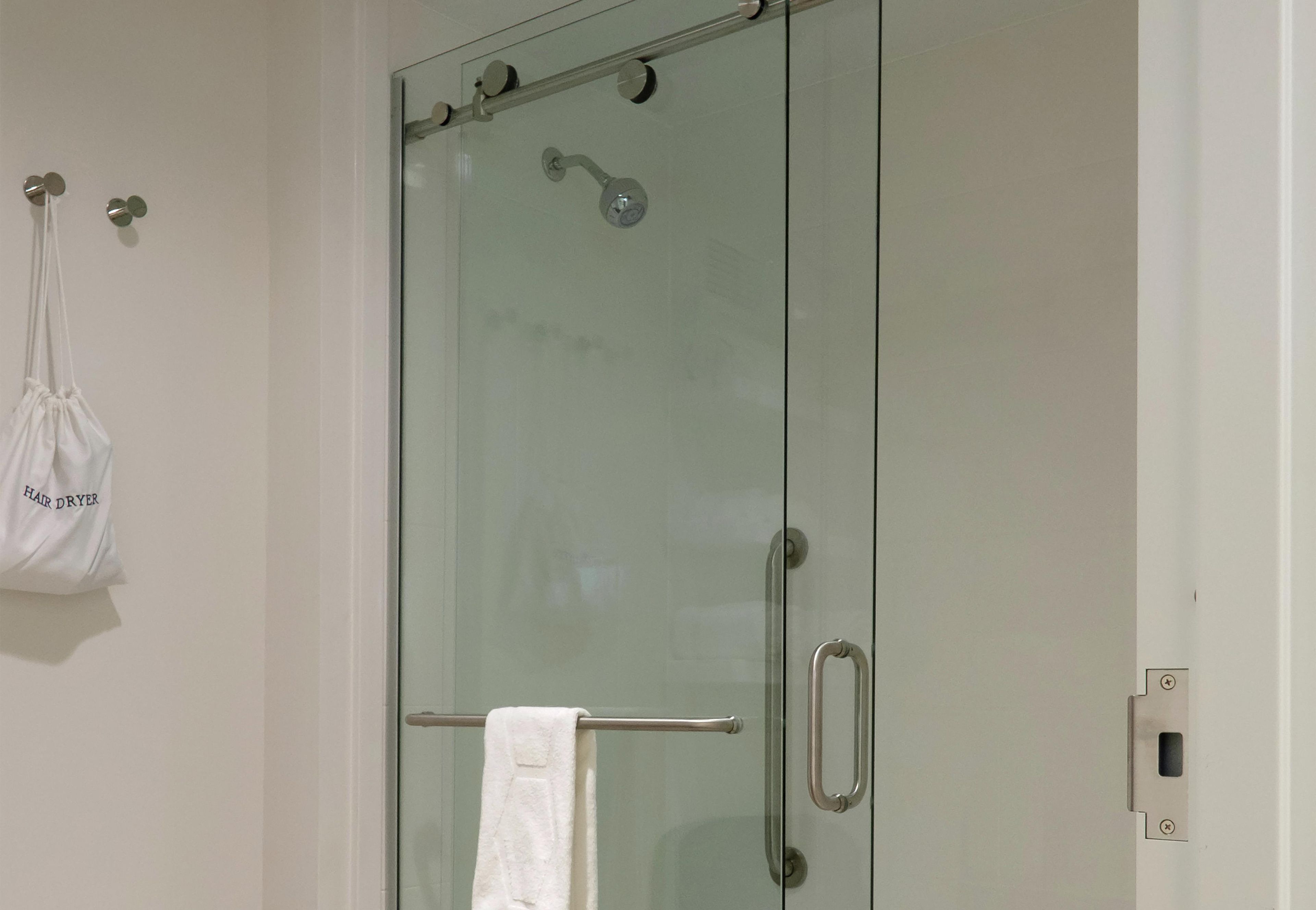 Une douche fermée par des parois en verre, avec une serviette accrochée à la poignée de la porte.