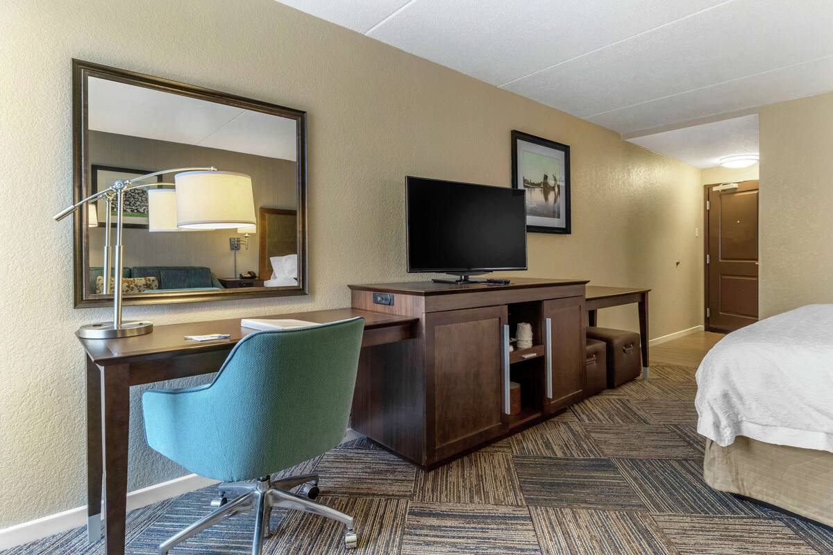 A hotel room with a desk, chair, television, and a bed.