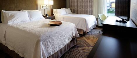 A hotel room with two beds, a desk, a TV, and a window with curtains.