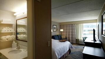 A hotel room with a bed, a desk, a chair, a bathroom with a sink and towel rack.