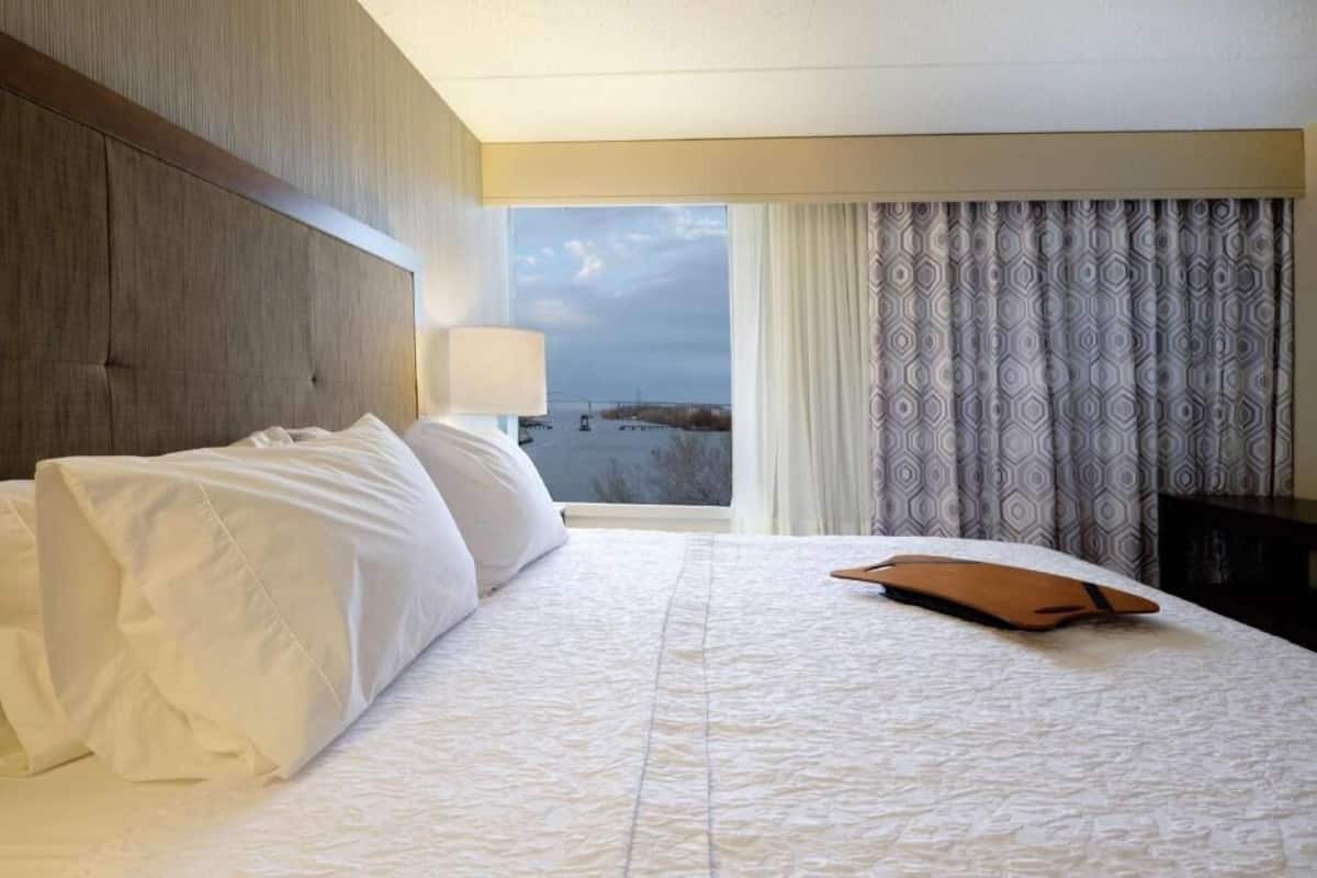 A hotel room with a large bed, a headboard, a window with curtains, and a view of the outside.