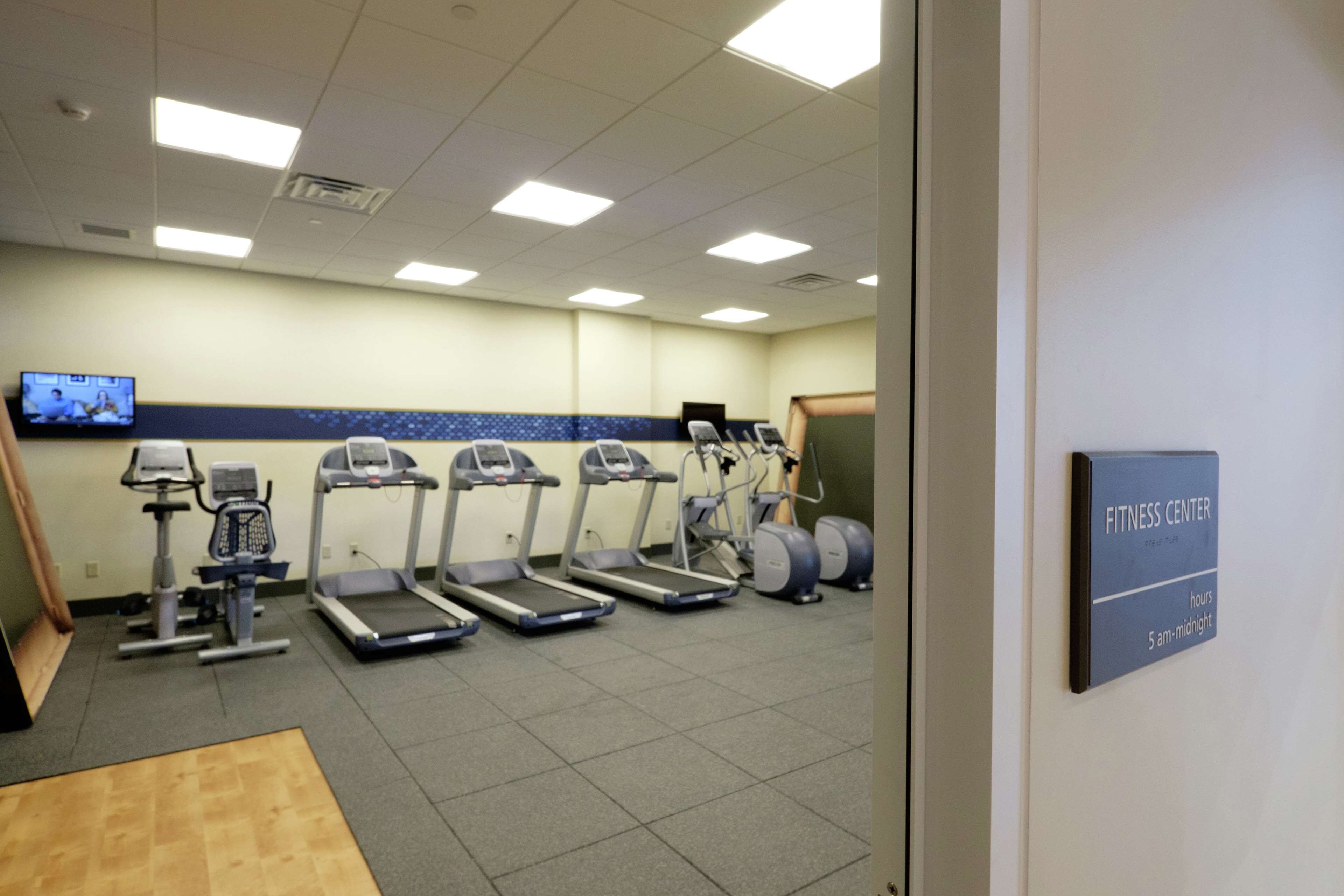 Een fitnessruimte met loopbanden, elliptische trainers en een televisiescherm.