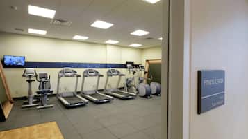Een fitnessruimte met loopbanden, elliptische trainers en een televisiescherm.